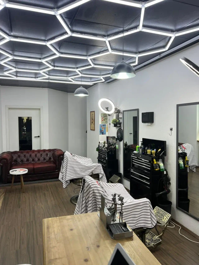 Im Milano Barbershop in Nürnberg: Barberstühle mit gestreiften Umhängen, Spiegel, Chesterfield-Sofa und Wabenlicht an der Decke